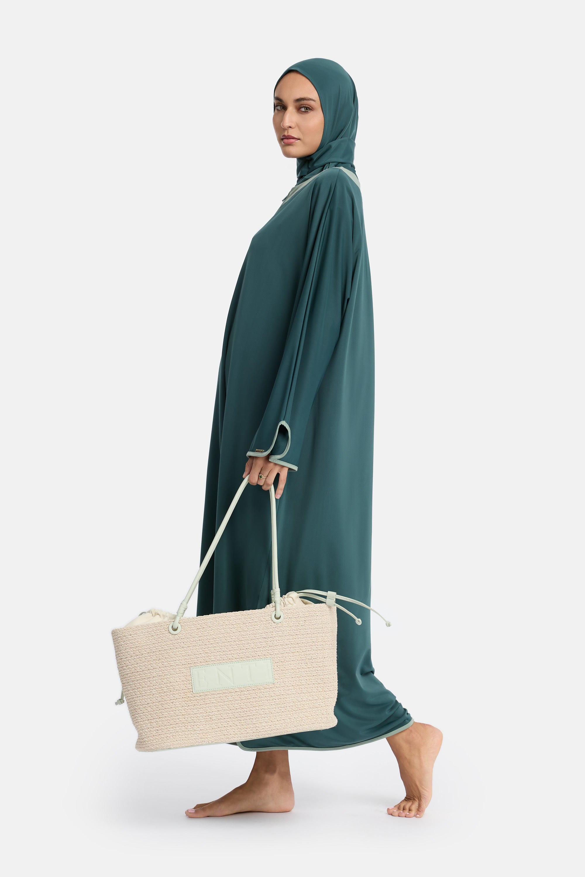 zij aanzicht van model die de modest burkini van het merk enti draag met de coverup jurk, instant swim hijab en de enti strandtas in de kleur minty green