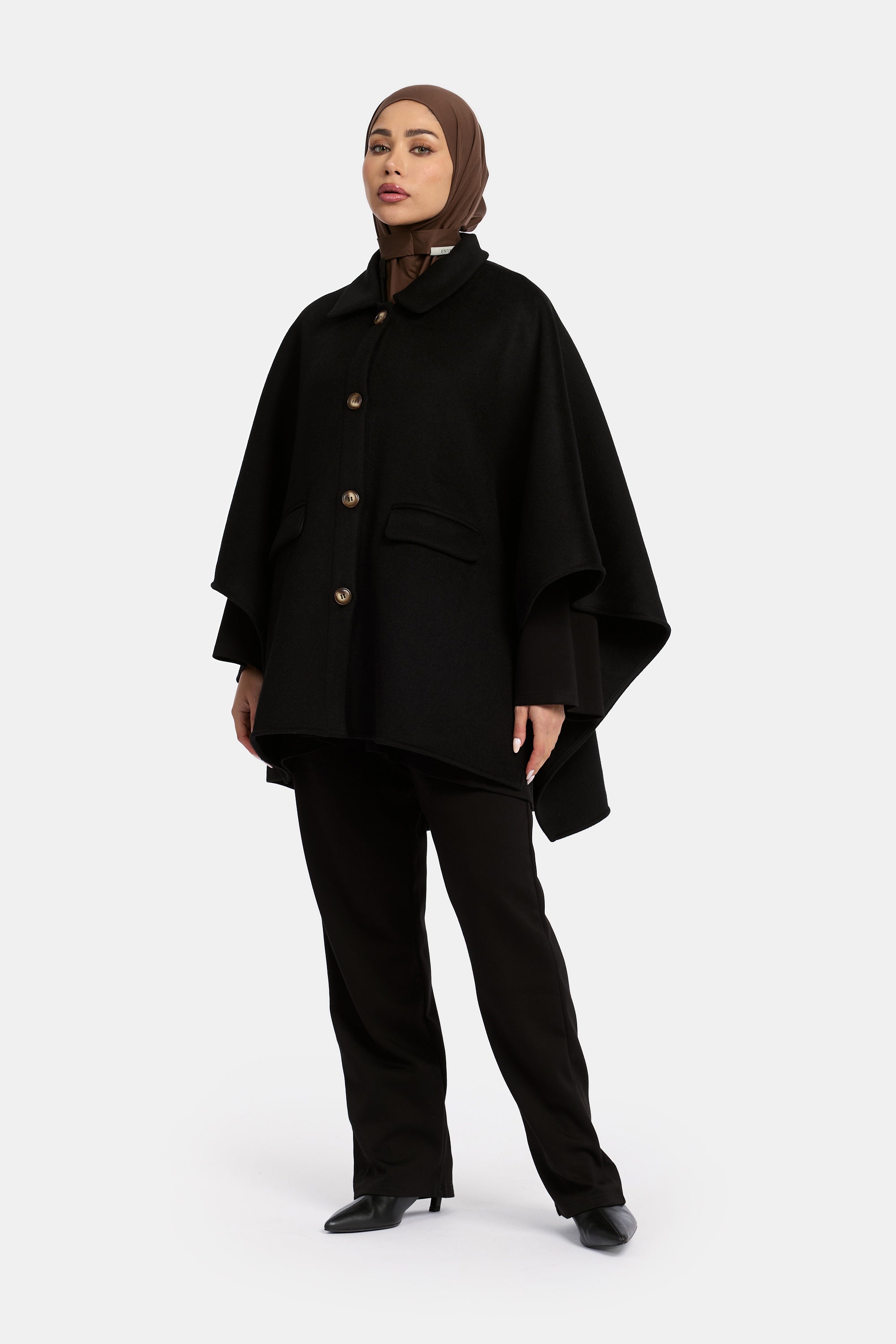 model draagt de wollen poncho van het modest merk enti in de kleur zwart en posseert