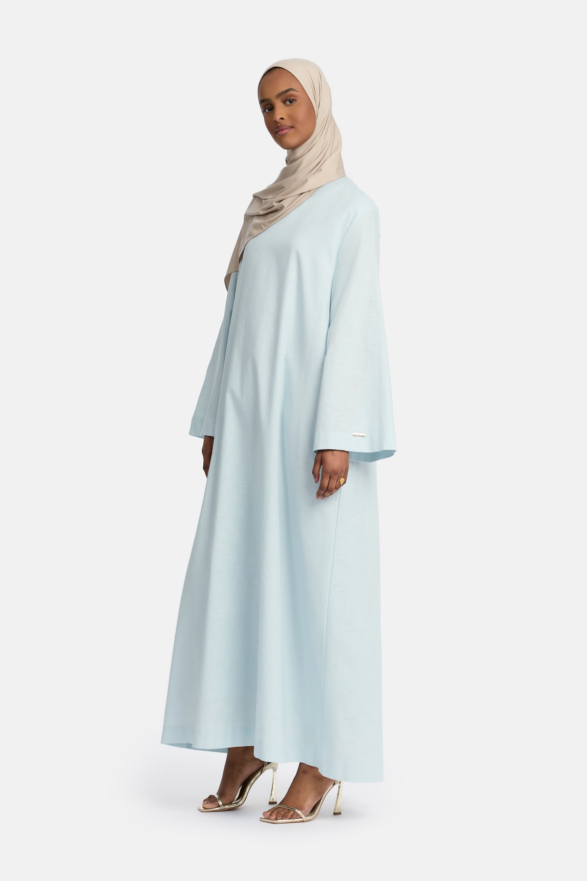 zij aanzicht van Model die draagt een modest linen loose dress van het merk enti in de kleur pastel blue