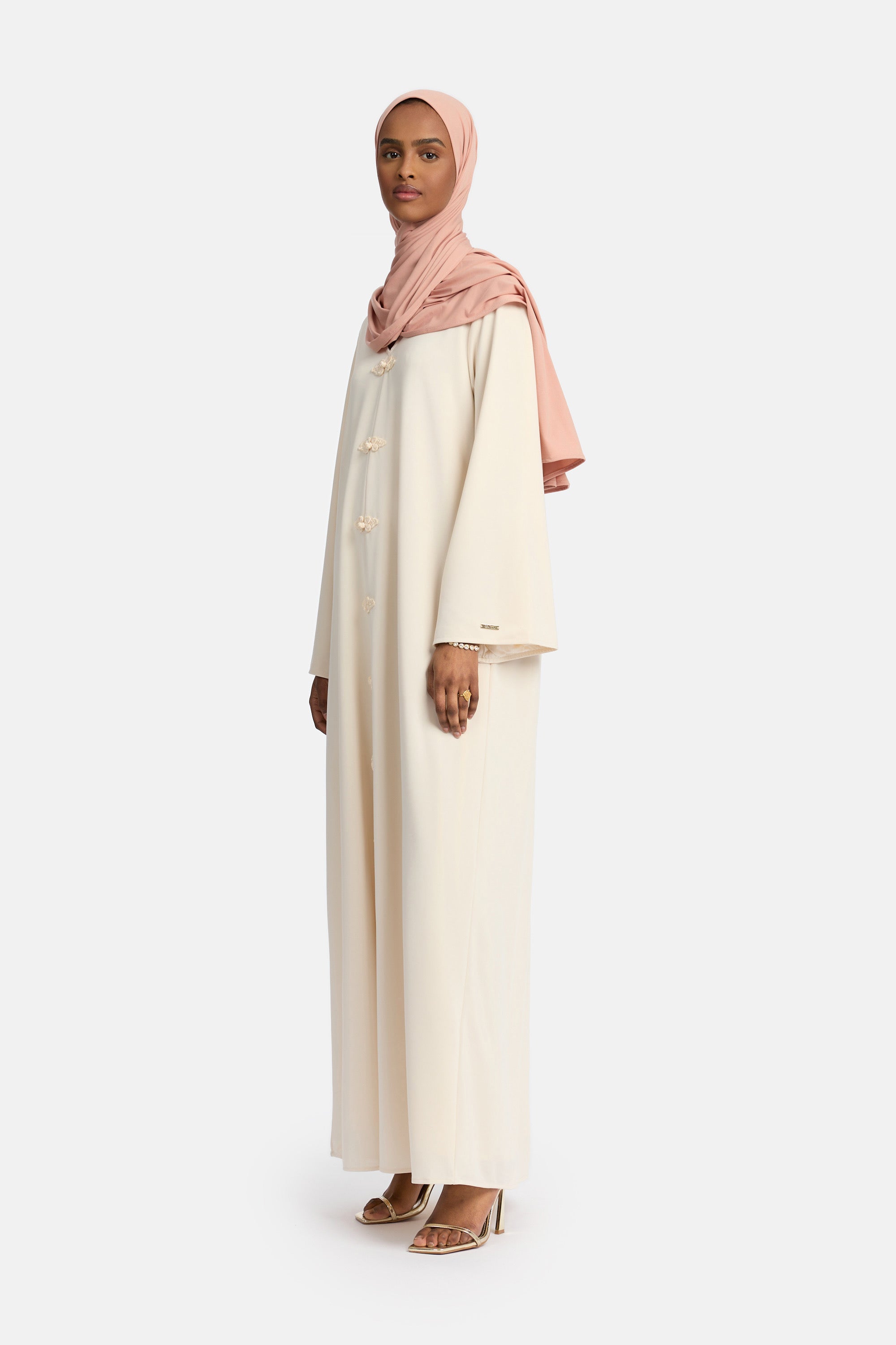 zij aanzicht van Model die draagt een modest kaftan dress van het merk enti in de kleur beige